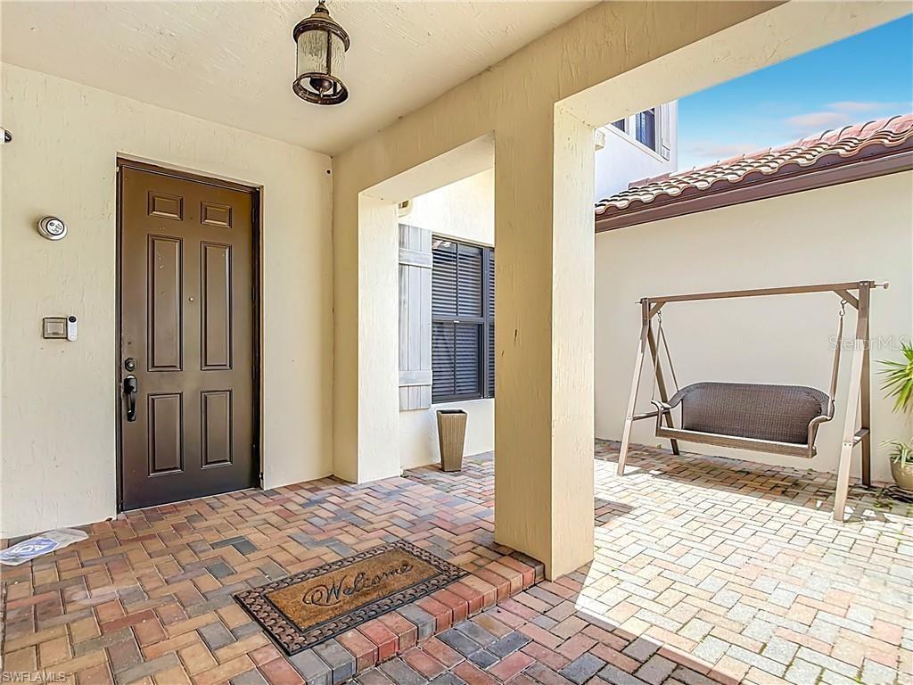A covered entryway features a brick-paver floor, a brown front door, and a porch swing — 5024 MILANO STREET, AVE MARIA, FL