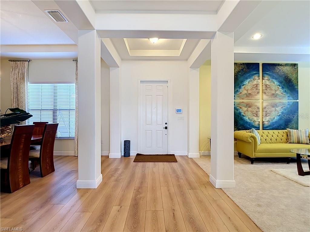 A bright entryway features light wood flooring, white columns, and a central white front door — 5024 MILANO STREET, AVE MARIA, FL