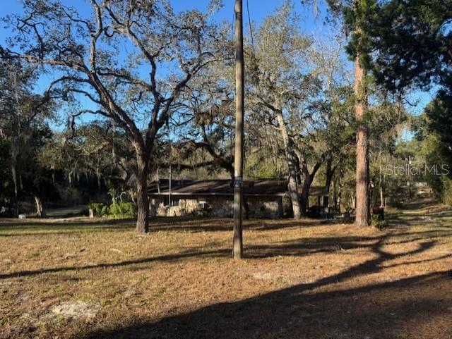 A stone-faced house sits among large trees in a grassy, sunlit yard — 12512 CR 685, WEBSTER, FL