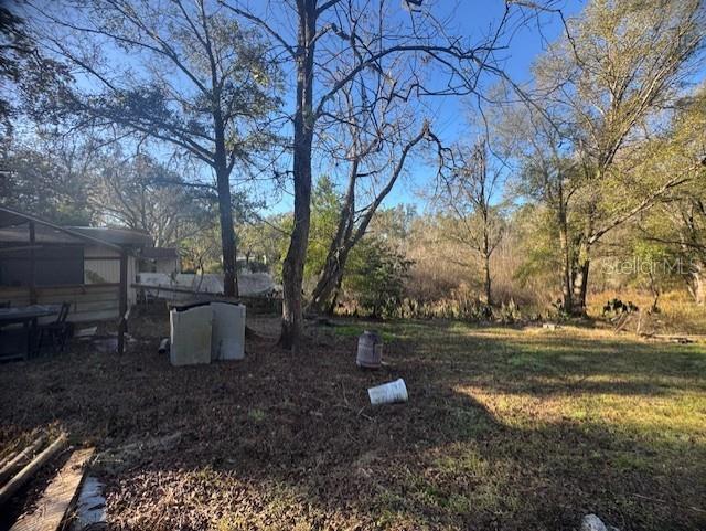 A backyard area features a covered patio, scattered debris, and several large, bare trees — 12512 CR 685, WEBSTER, FL