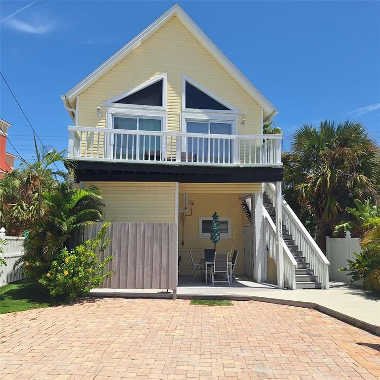 A yellow two-story house features an elevated deck, outdoor stairs, and a paved driveway — 13202 GULF BOULEVARD, MADEIRA BEACH, FL