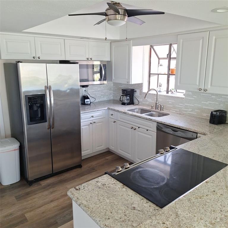 A kitchen features white cabinets, stainless steel appliances, granite countertops, and a wood-look floor — 13202 GULF BOULEVARD, MADEIRA BEACH, FL