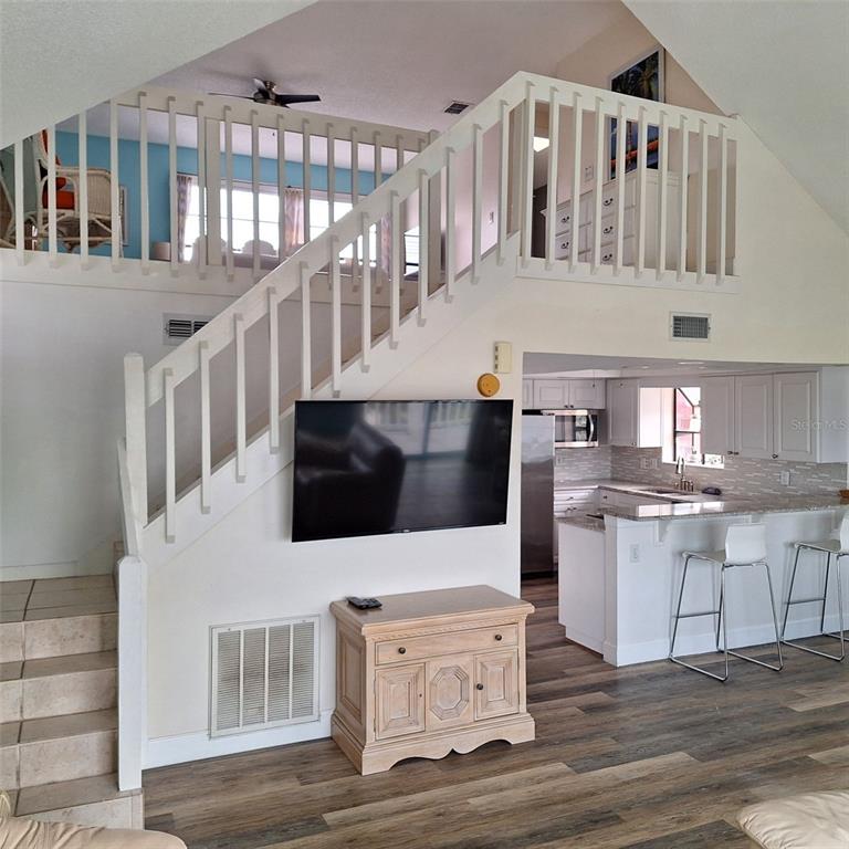 A living room with a staircase, a wall-mounted television, and an open kitchen with bar seating — 13202 GULF BOULEVARD, MADEIRA BEACH, FL
