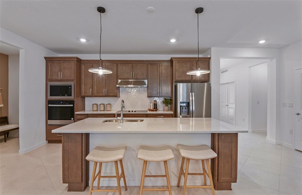 A modern kitchen features wood cabinets, a quartz-topped island with three stools, and stainless appliances — 3656 OBSIDIAN DRIVE, SPRING HILL, FL