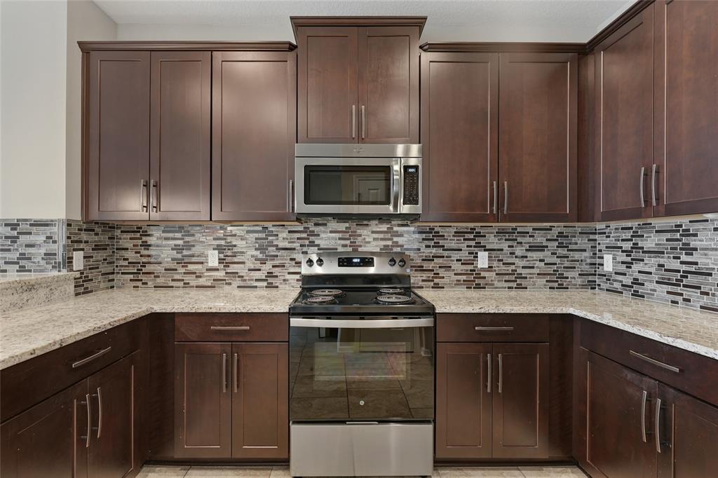 A kitchen features dark wood cabinets, stainless steel appliances, granite countertops, and a mosaic tile backsplash — 15613 ORANGE HARVEST LOOP, WINTER GARDEN, FL