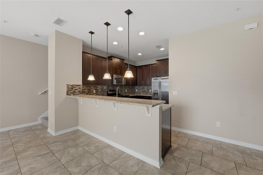 A kitchen features dark wood cabinets, granite countertops, a tiled backsplash, and three pendant lights — 15613 ORANGE HARVEST LOOP, WINTER GARDEN, FL