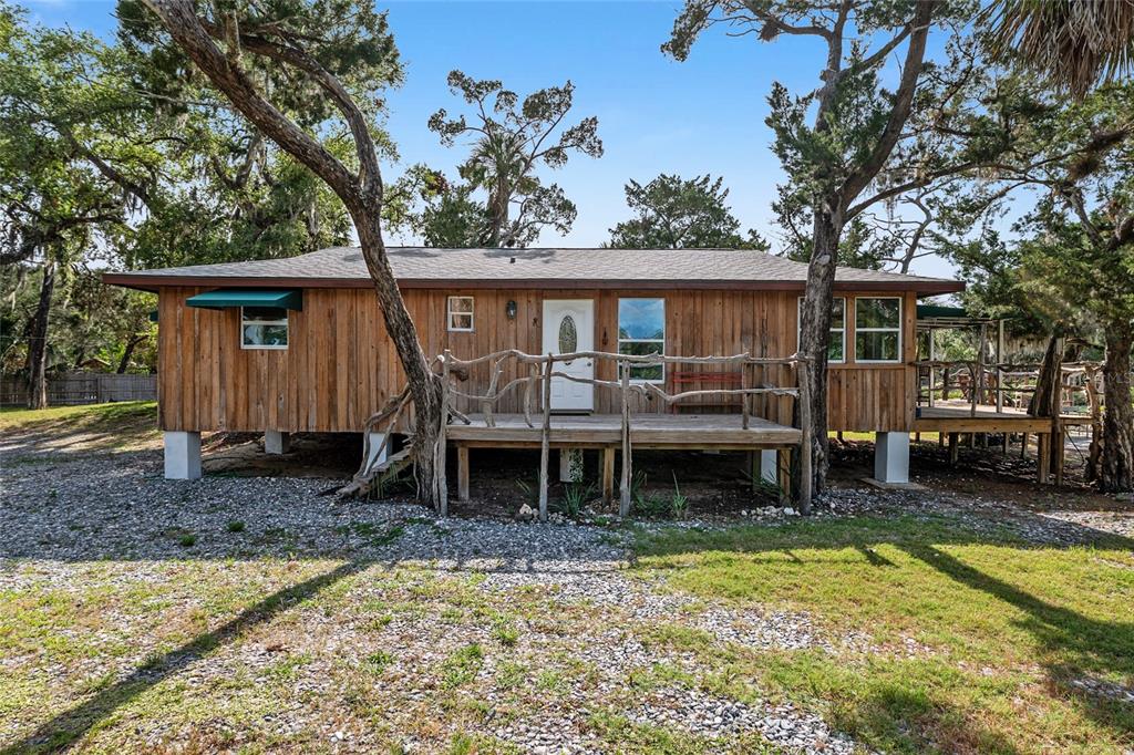 A wood-sided house on stilts features a rustic branch railing on the front deck — 1326 S ESTUARY, CRYSTAL RIVER, FL
