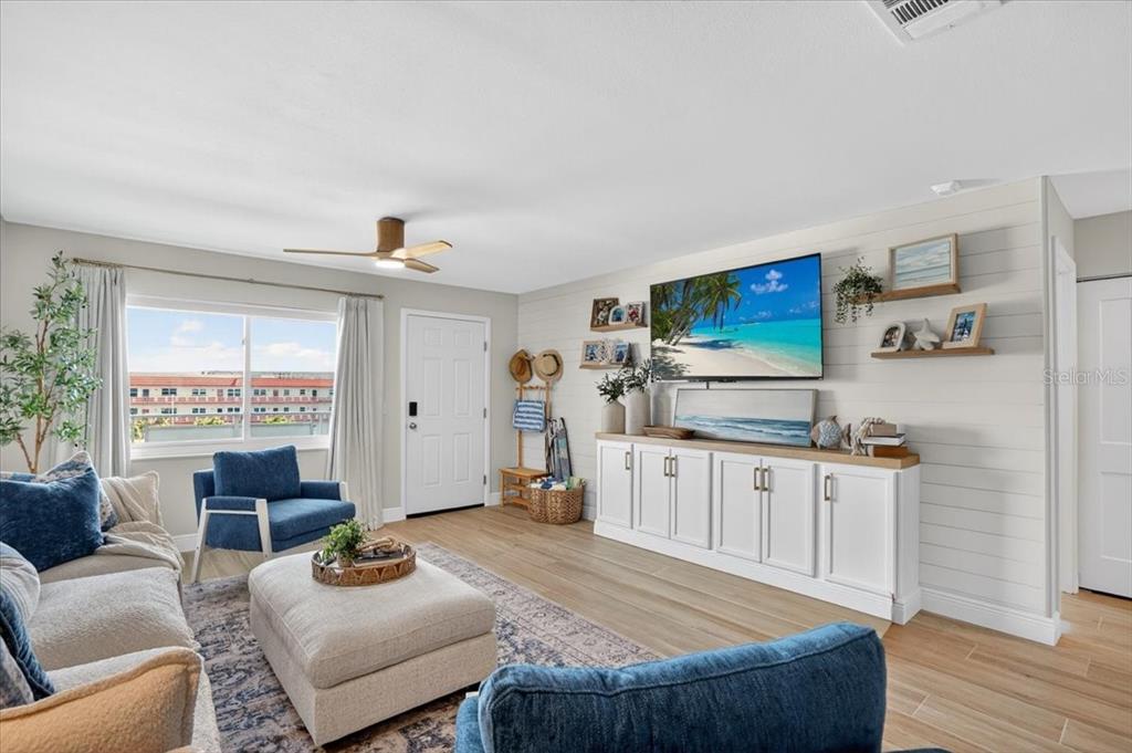 A living room features a white media console, a wall-mounted television, and blue accent furniture — 2960 59TH STREET S UNIT 310, GULFPORT, FL
