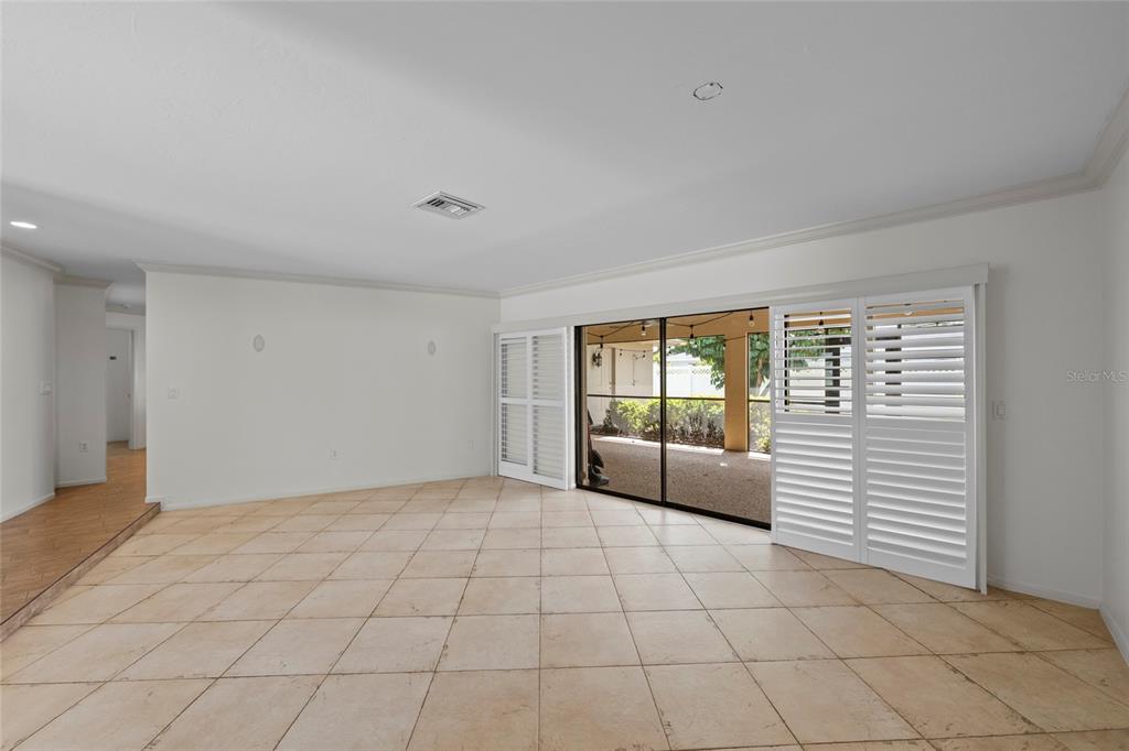 A spacious room with beige tile flooring, white walls, and sliding glass doors with shutters — 1252 WATERSIDE LANE, VENICE, FL