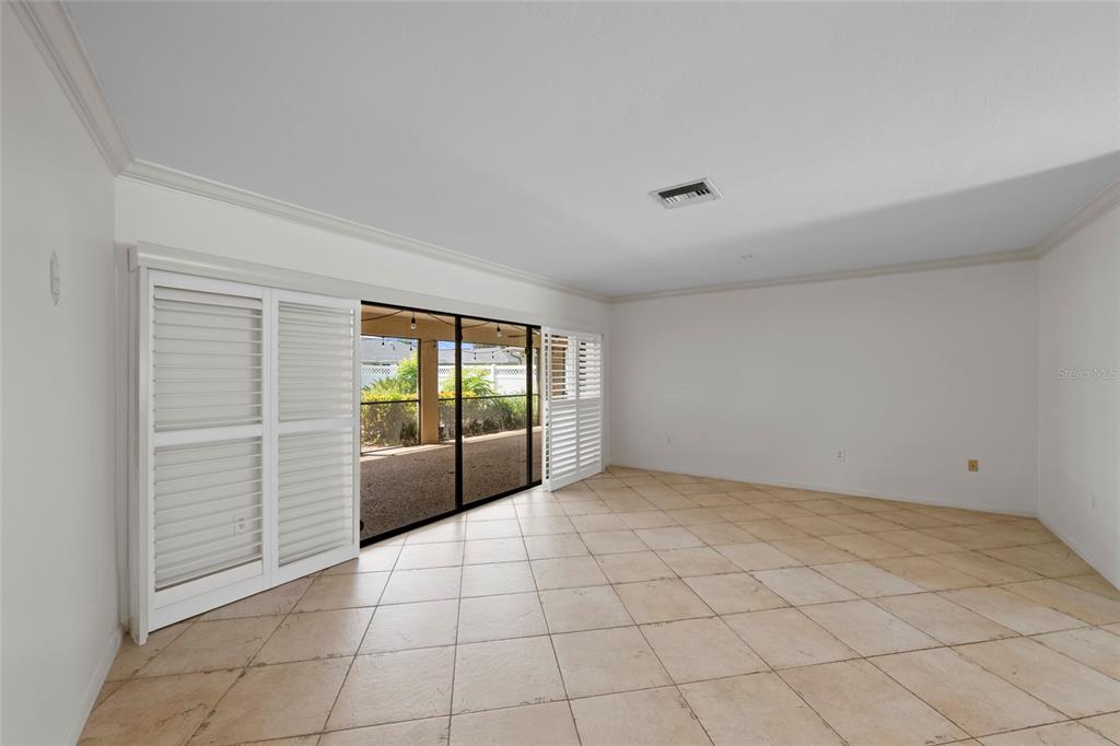 A spacious room with beige tile flooring, white walls, and sliding glass doors with shutters — 1252 WATERSIDE LANE, VENICE, FL