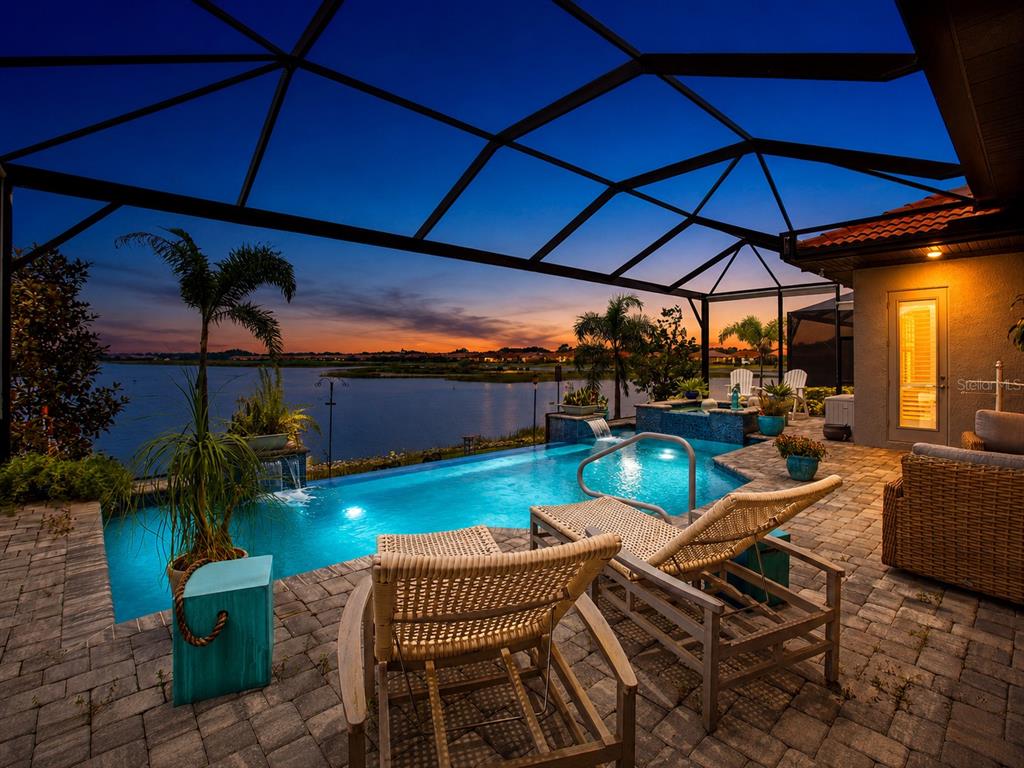 A screened-in patio features a swimming pool, hot tub, and lounge chairs overlooking a lake — 617 MARAVIYA BOULEVARD, NOKOMIS, FL