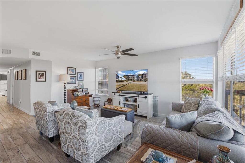 A living room features light wood-look flooring, two patterned armchairs, a gray sofa, and a television — 11 OLD MILL DRIVE UNIT 9C, CEDAR KEY, FL