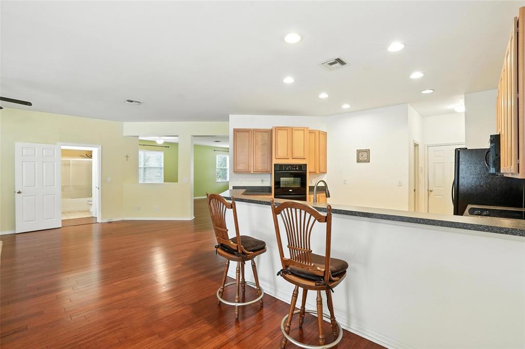 A kitchen with light wood cabinets and a breakfast bar overlooks a hardwood-floored living area — 10043 WINDING RIVER ROAD, PUNTA GORDA, FL