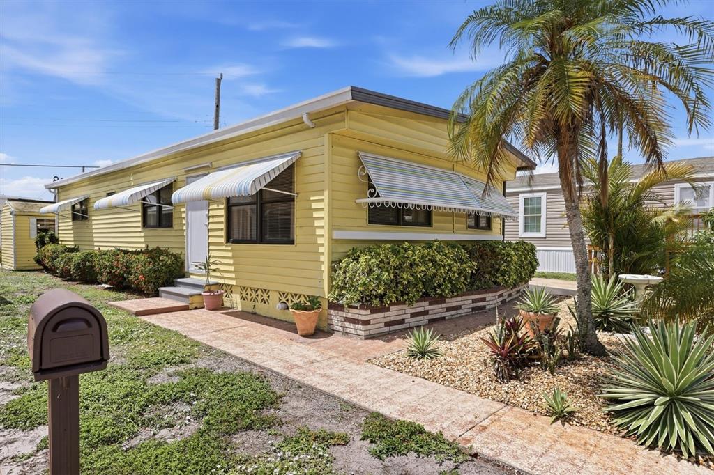 A yellow mobile home with striped window awnings, a brick walkway, and a palm tree — 4109 12TH STREET E, ELLENTON, FL