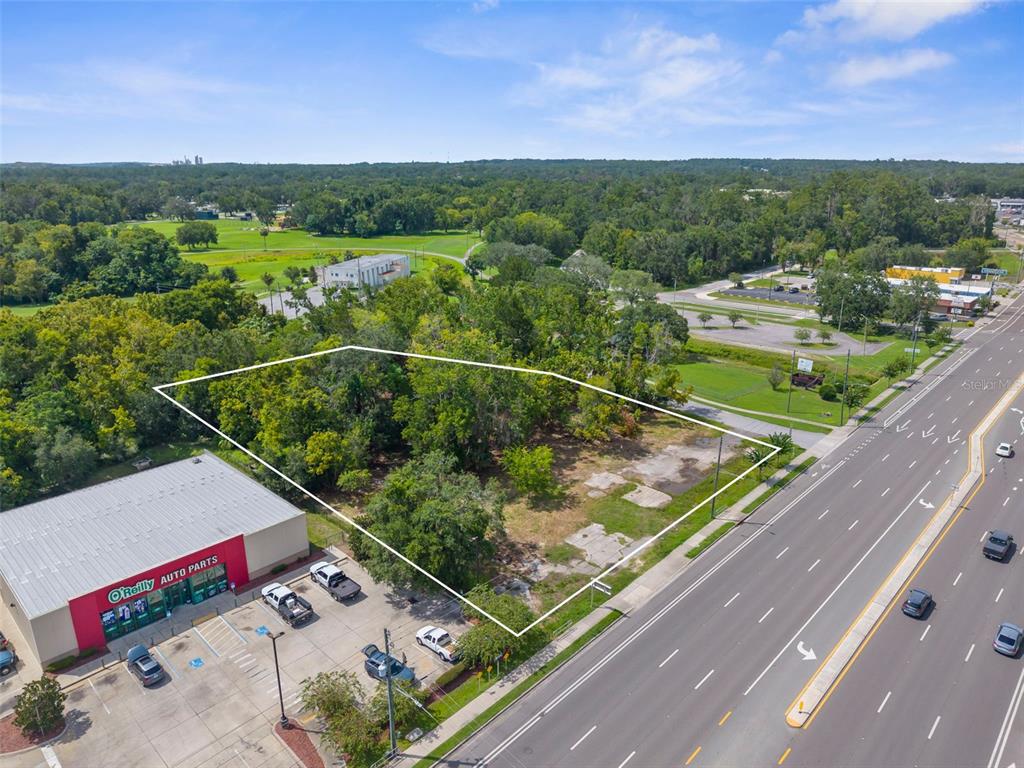 An aerial view shows a vacant, wooded lot bordered by a road and a commercial building — 802 S BROAD STREET, BROOKSVILLE, FL