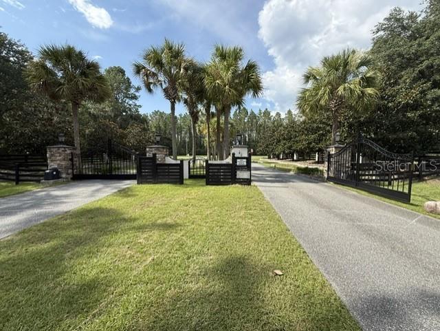 A paved driveway leads through an open black metal gate flanked by stone pillars and palms — TBD NW 148TH LANE, WILLISTON, FL