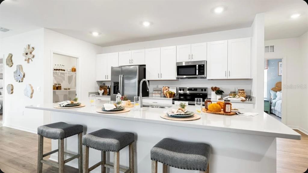 A modern kitchen features white cabinets, stainless steel appliances, and a large quartz-topped island — 7417 FIELDSTONE DRIVE, GROVELAND, FL