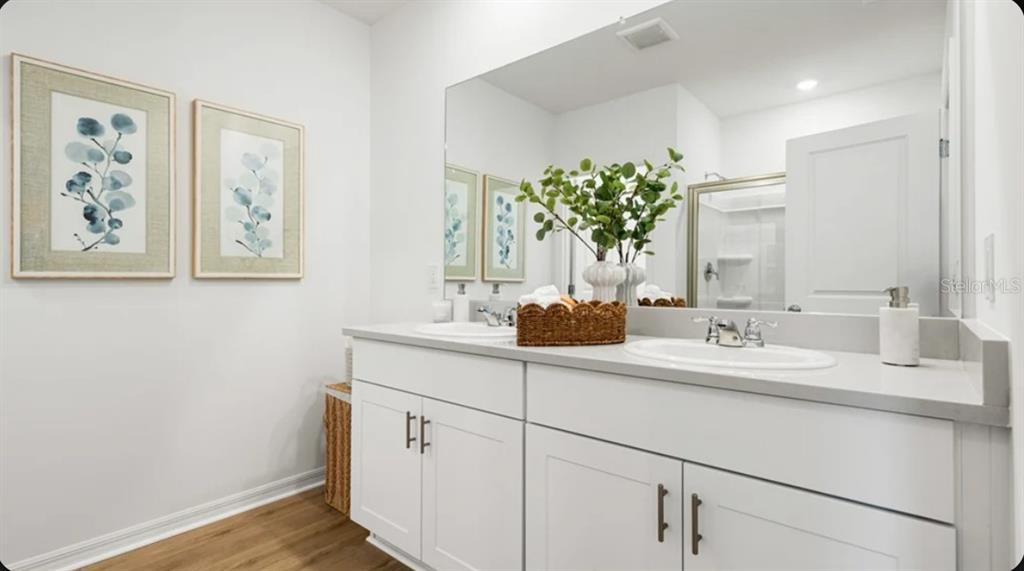 A bathroom features a double vanity with white cabinets, a large mirror, and framed artwork — 7417 FIELDSTONE DRIVE, GROVELAND, FL