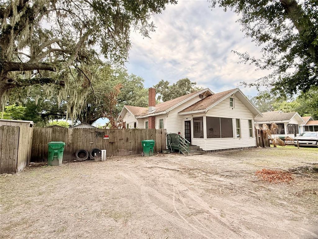 A white house with a screened porch and a brick chimney sits behind a wooden fence — 208 3RD STREET, WINTER GARDEN, FL