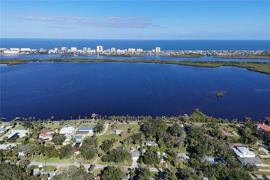 An aerial view shows a residential neighborhood bordering a large lake with a distant coastline — 5040 RIVERSIDE DRIVE, PORT ORANGE, FL