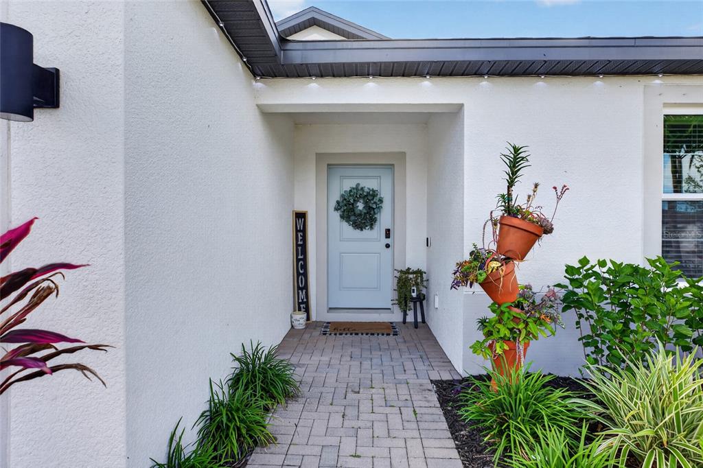 A paved walkway leads to a light blue front door with a wreath and welcome sign — 5316 PATANO LOOP, PALMETTO, FL
