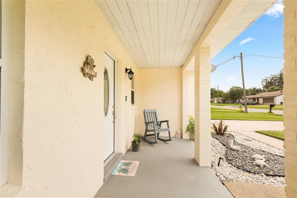 A covered front porch features a rocking chair, a welcome mat, and a white door — 38 LAUREL OAKS CIRCLE, ORMOND BEACH, FL