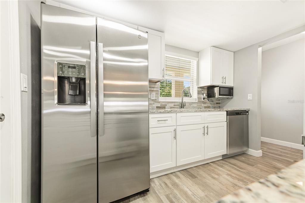 A kitchen features stainless steel appliances, white cabinetry, granite countertops, and light wood-look flooring — 38 LAUREL OAKS CIRCLE, ORMOND BEACH, FL