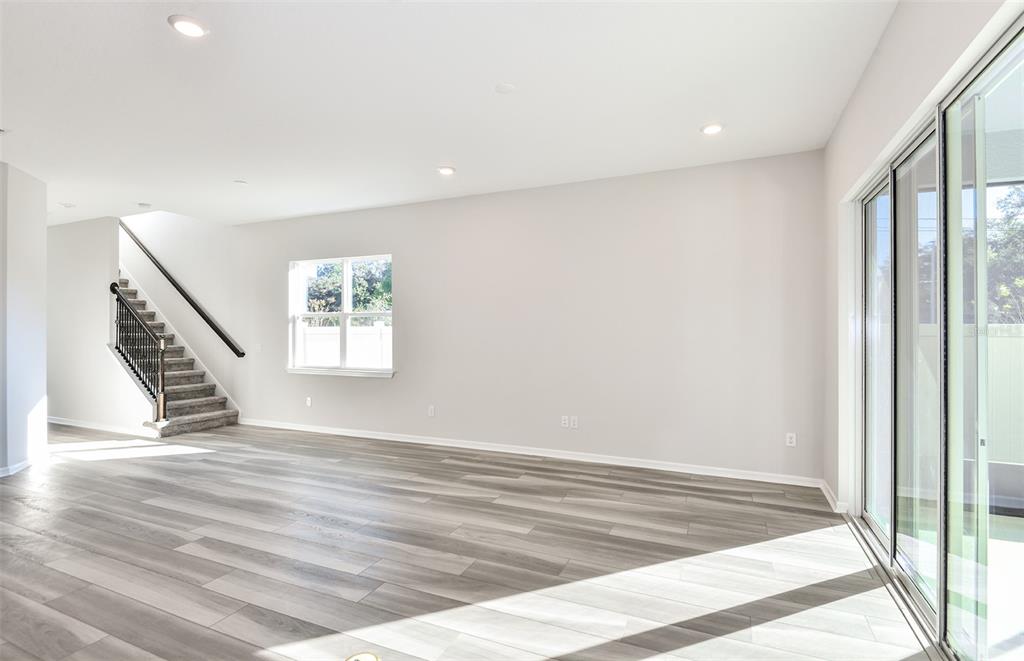 An empty living room features gray wood-look flooring, a staircase with a railing, and sliding doors — 9853 TRELLIS VINE WAY, PARRISH, FL
