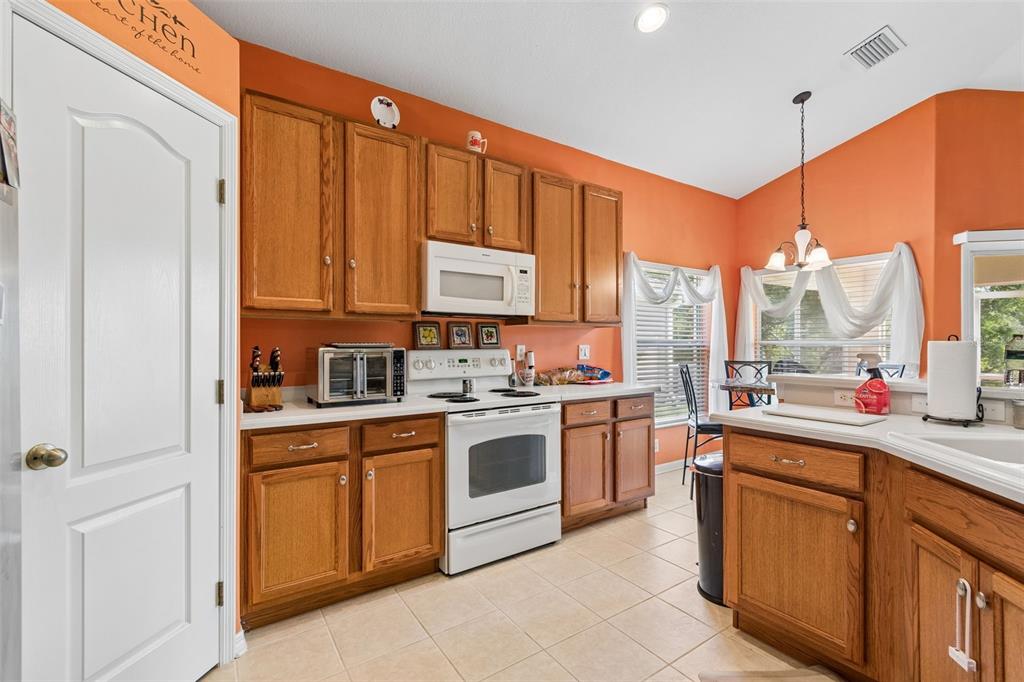 A kitchen with orange walls, wood cabinets, white appliances, and light-colored tile flooring — 4017 LANGDRUM DRIVE, WESLEY CHAPEL, FL