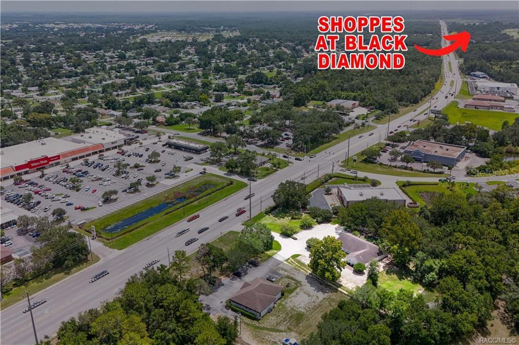 An aerial view shows a commercial shopping center, a multi-lane road, and surrounding wooded areas — 3628 N LECANTO HIGHWAY, BEVERLY HILLS, FL