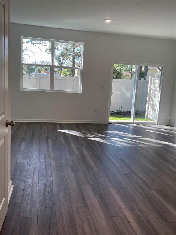 An empty room features wood-look flooring, a window, and a sliding glass door to a yard — 6157 DAERR RIDGE UNIT 6157, ZEPHYRHILLS, FL