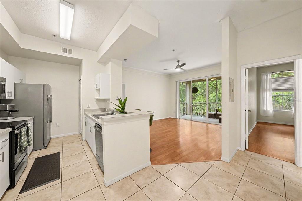 A kitchen with tile floors and a stainless steel refrigerator opens to a wood-floored living area — 17108 CARRINGTON PARK DR UNIT 722, TAMPA, FL