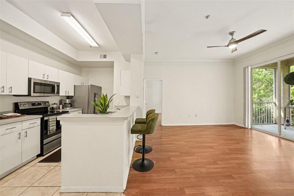 A kitchen with white cabinets and stainless appliances opens to a living area with balcony — 17108 CARRINGTON PARK DR UNIT 722, TAMPA, FL