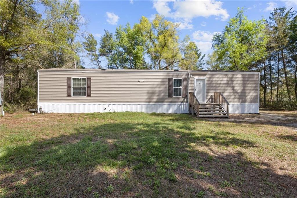 A single-story manufactured home with tan siding and white skirting sits on a grassy lot — 11061 NE 65TH LANE, WILLISTON, FL
