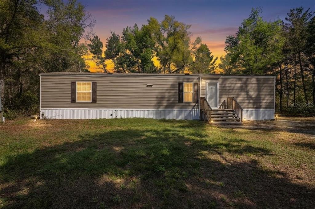 A single-story manufactured home with tan siding sits on a grassy lot at sunset — 11061 NE 65TH LANE, WILLISTON, FL