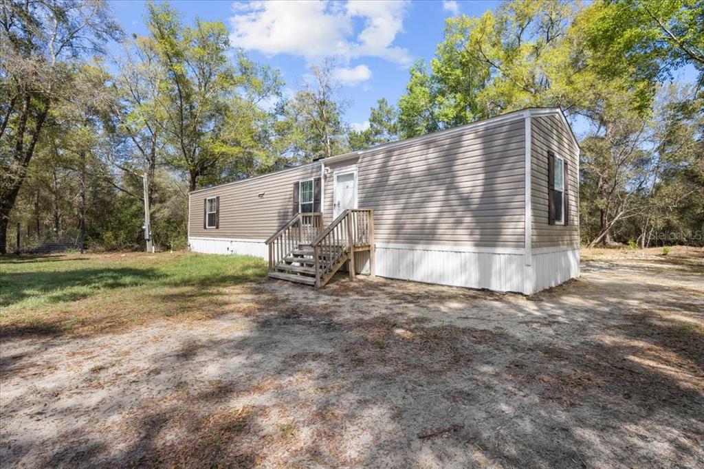 A single-story manufactured home with tan siding and a wooden staircase sits on a lot — 11061 NE 65TH LANE, WILLISTON, FL