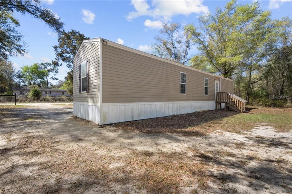 A tan mobile home with white skirting sits on a sandy lot among trees — 11061 NE 65TH LANE, WILLISTON, FL