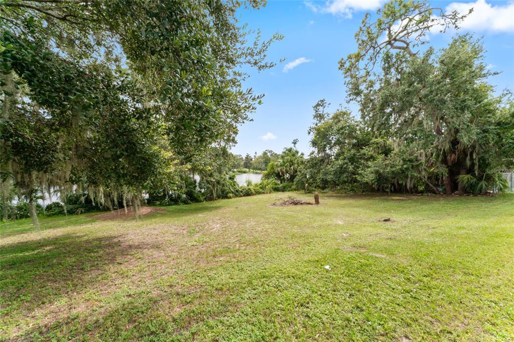 A grassy, sloping backyard leads toward a lake surrounded by mature trees — 0 RIVERHILLS DRIVE, TEMPLE TERRACE, FL