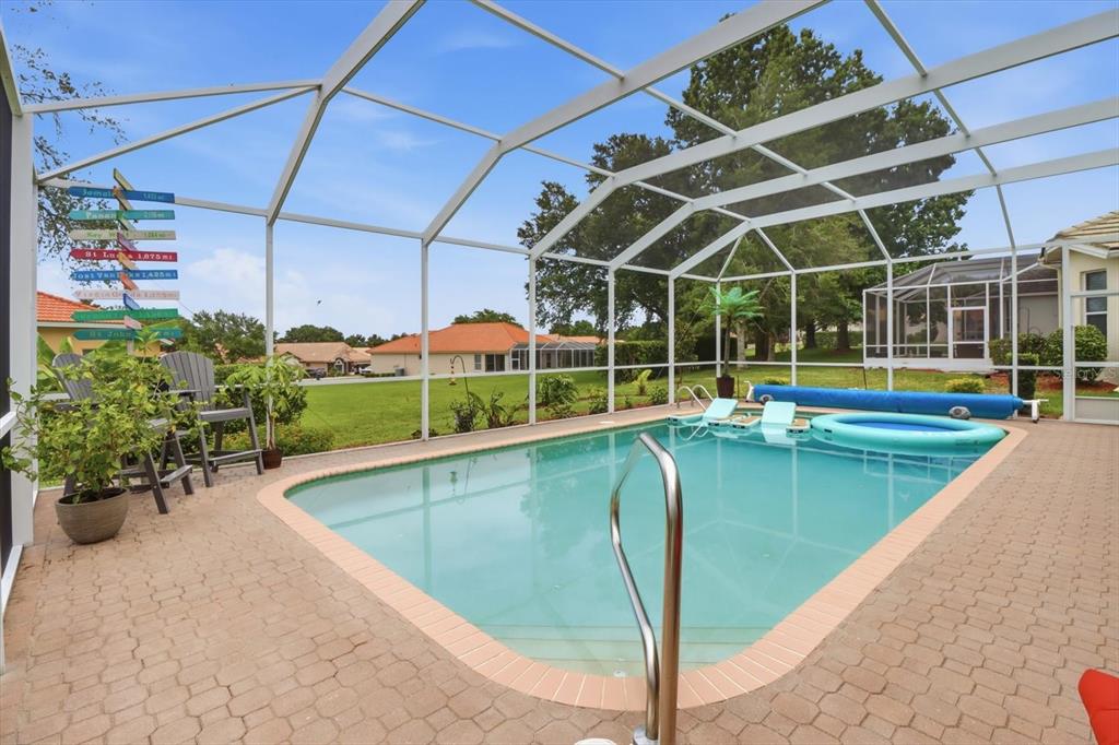 A screened-in swimming pool patio features a paved deck, lounge chairs, and a directional signpost — 1096 W DIAMOND SHORE LOOP, HERNANDO, FL