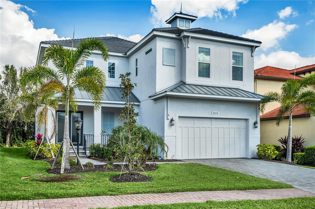 A two-story light gray house with a metal roof, a garage, and palm trees — 5215 TITLE ROW DRIVE, BRADENTON, FL