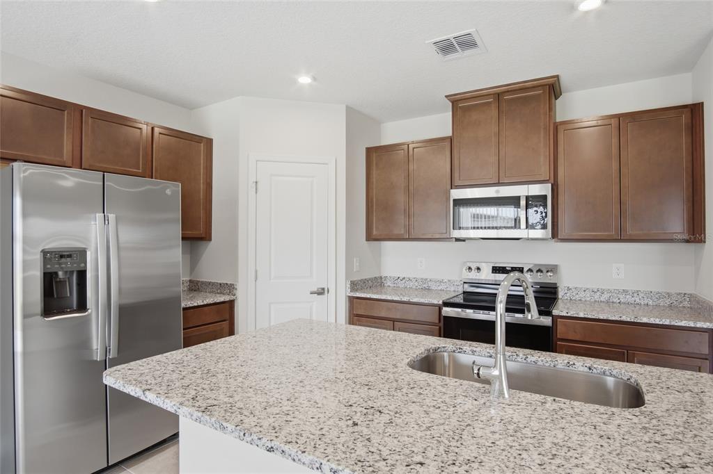 A kitchen features dark wood cabinets, granite countertops, stainless steel appliances, and a central island — 724 CANTABERRY DRIVE, DUNDEE, FL
