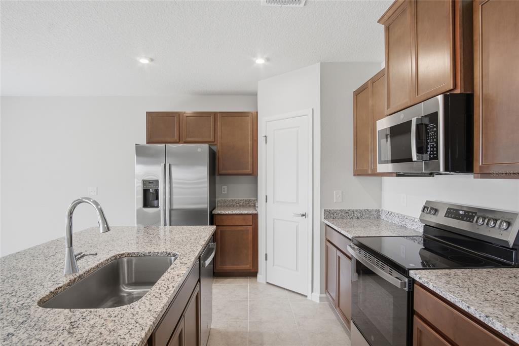 A kitchen with granite countertops, stainless steel appliances, and brown wooden cabinetry — 724 CANTABERRY DRIVE, DUNDEE, FL