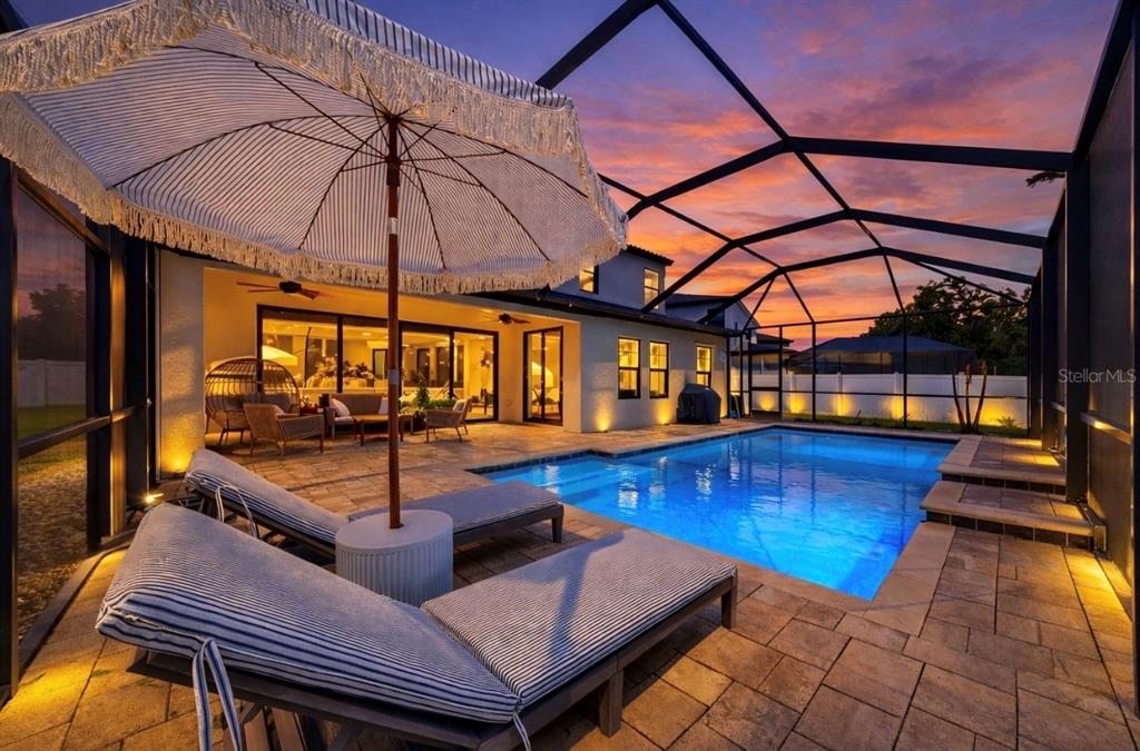 A screened-in patio features a swimming pool, lounge chairs, and a striped umbrella at sunset — 13036 PENNYBROOK DRIVE, RIVERVIEW, FL