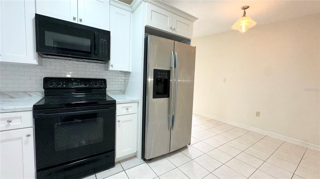 A kitchen features white cabinets, stainless steel appliances, a black stove, and tiled flooring — 4110 ALVERADO STREET, ORLANDO, FL