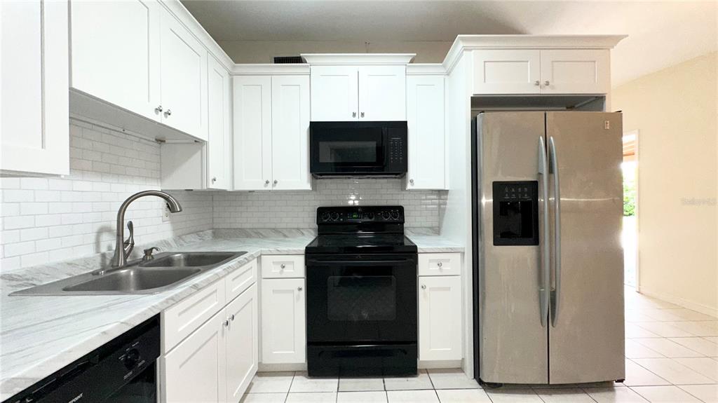 A kitchen features white cabinets, stainless steel appliances, a black stove, and a subway tile backsplash — 4110 ALVERADO STREET, ORLANDO, FL