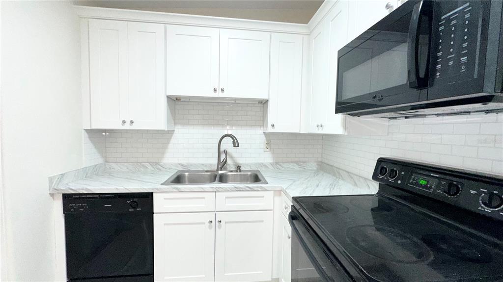 A kitchen features white cabinets, marble-patterned countertops, a subway tile backsplash, and black appliances — 4110 ALVERADO STREET, ORLANDO, FL