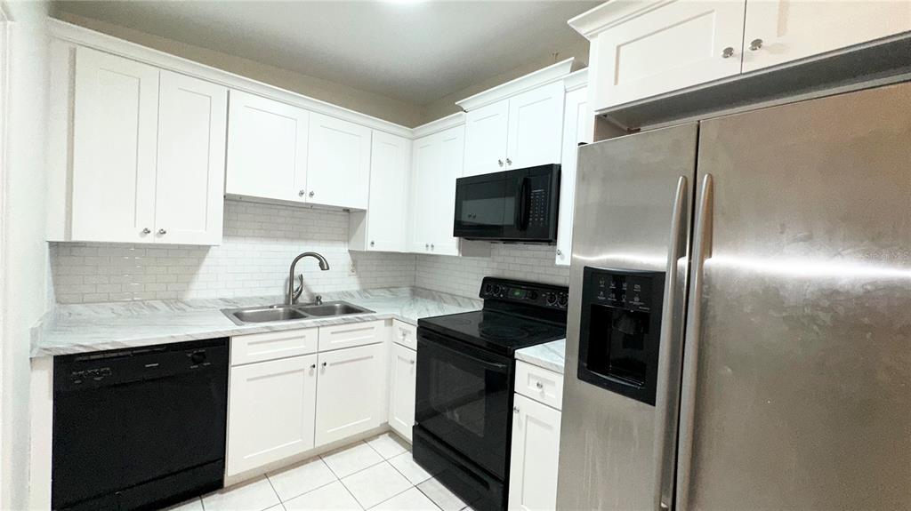 A kitchen features white cabinets, marble-look countertops, a subway tile backsplash, and black appliances — 4110 ALVERADO STREET, ORLANDO, FL