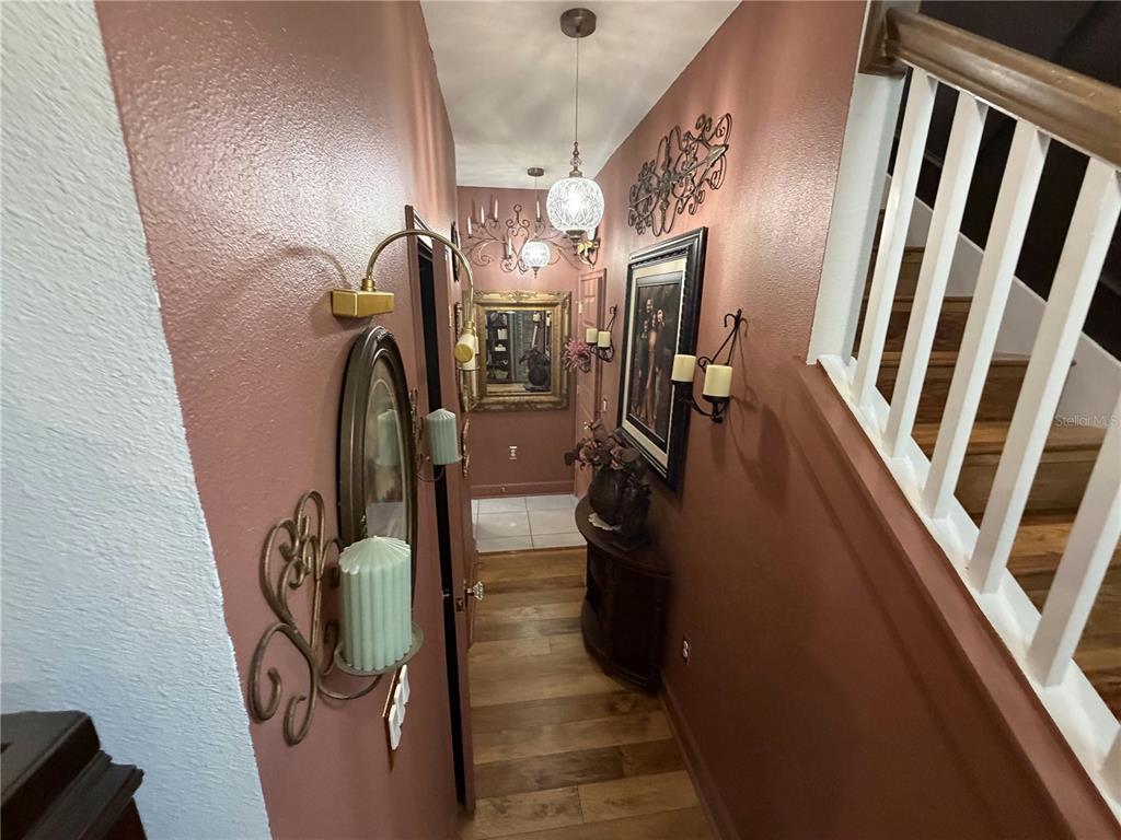 A narrow hallway features reddish-brown walls, wood flooring, wall sconces, and a staircase railing — 3795 SAGEFIELD DRIVE, HARMONY, FL