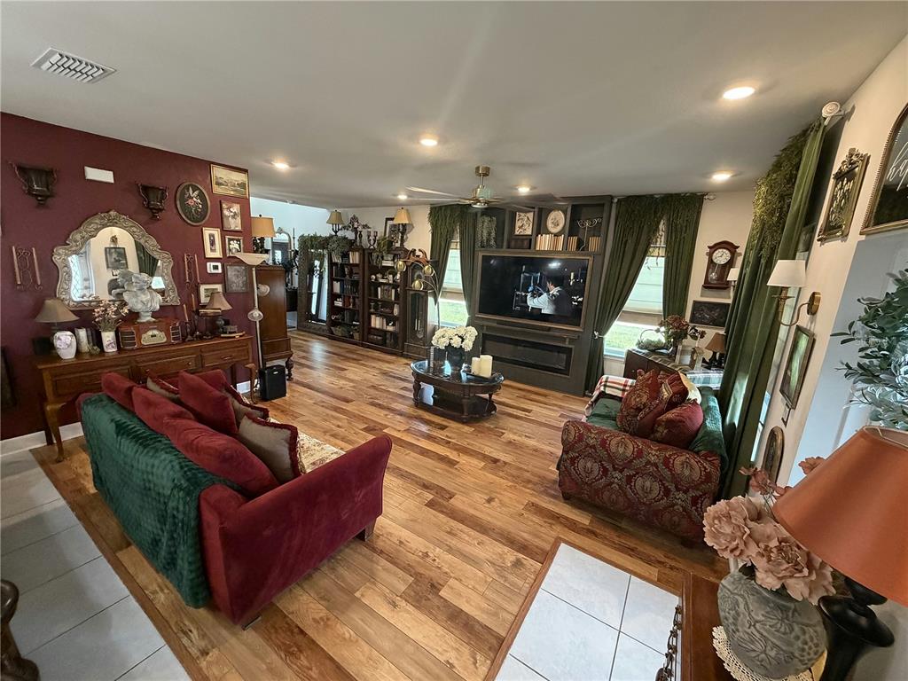 A living room features hardwood floors, a red sofa, a television console, and dark curtains — 3795 SAGEFIELD DRIVE, HARMONY, FL