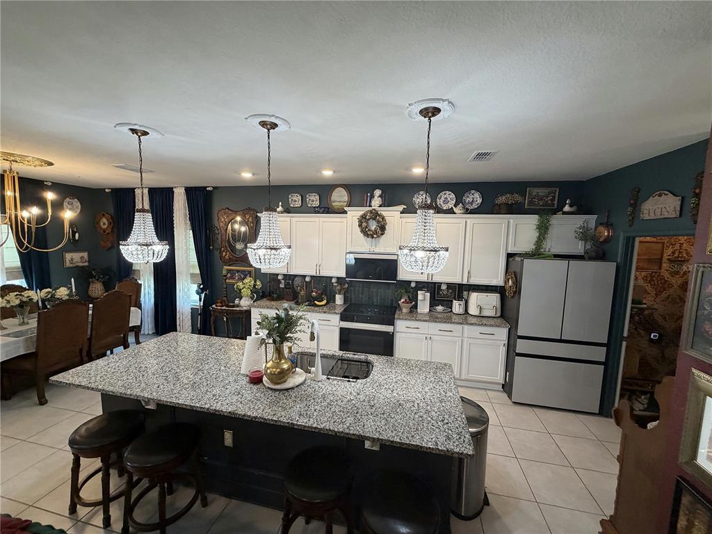 A kitchen features a granite-topped island, white cabinetry, stainless steel appliances, and crystal pendant lights — 3795 SAGEFIELD DRIVE, HARMONY, FL